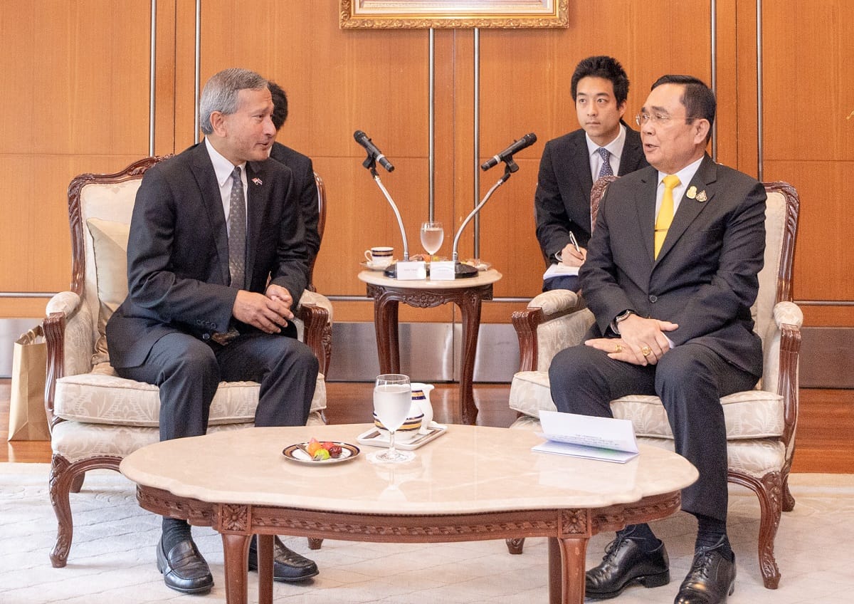 Two men in suits seated facing each other with aide behind; mics, documents, snacks on tables.